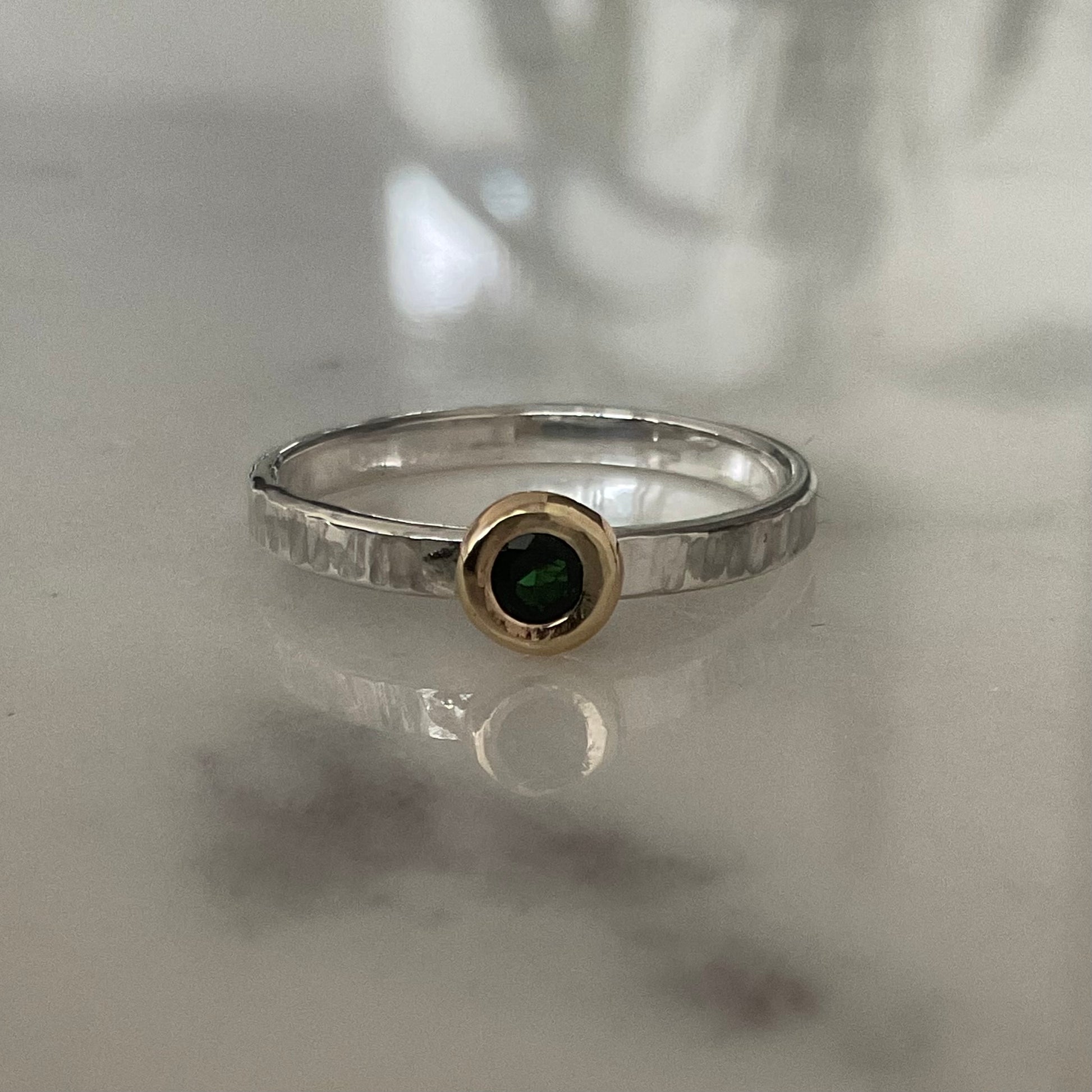 Silver ring with a green gemstone on a reflective surface