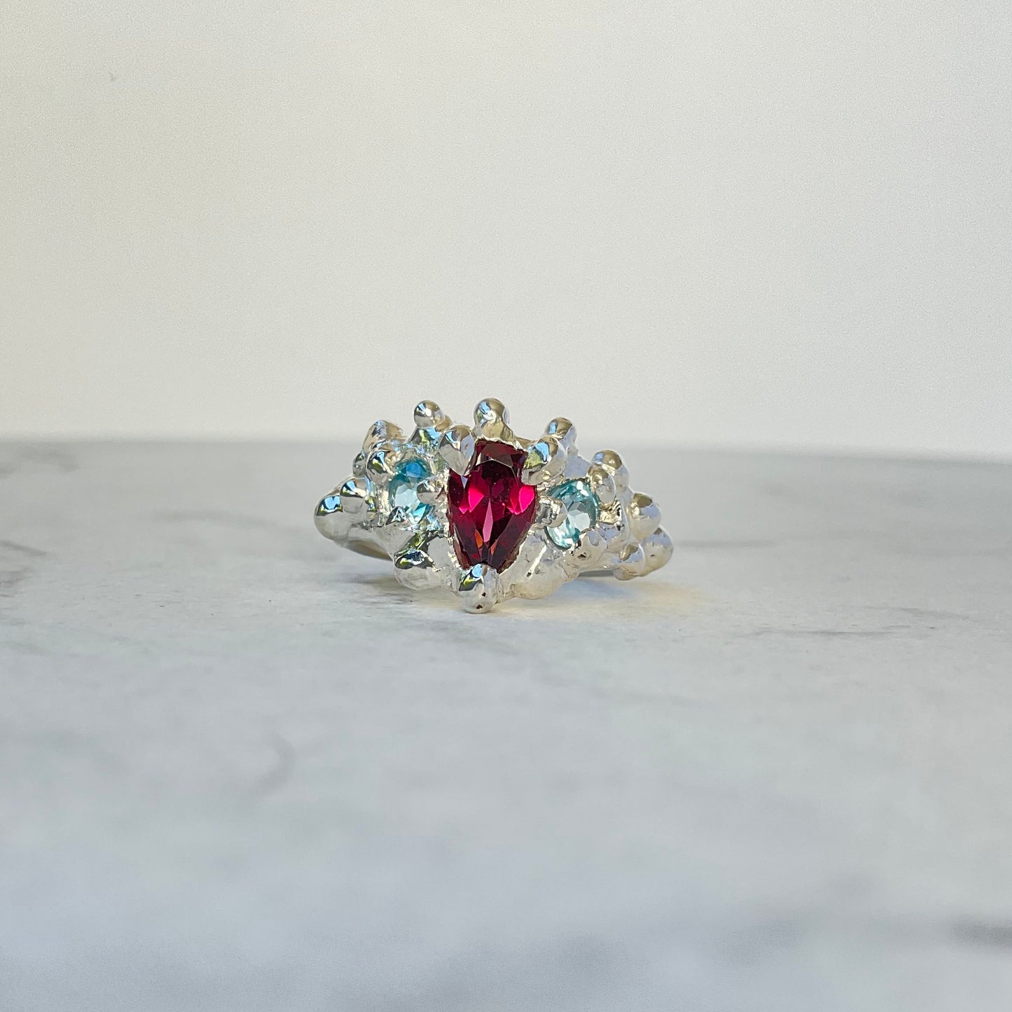 Pear shaped pink garnet with swiss blue topaz accent stones in a molten silver style ring.
