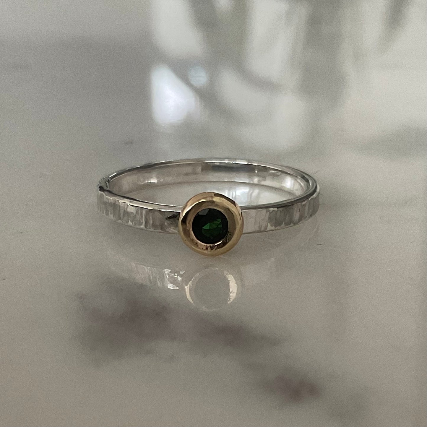 Silver ring with a green gemstone on a reflective surface