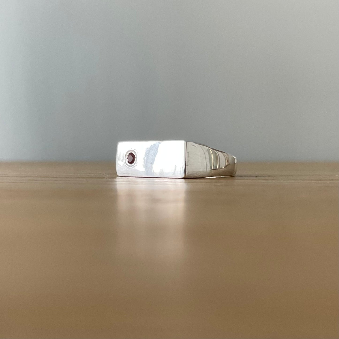 Silver ring with a red sapphire gemstone on a wooden surface with a gray background