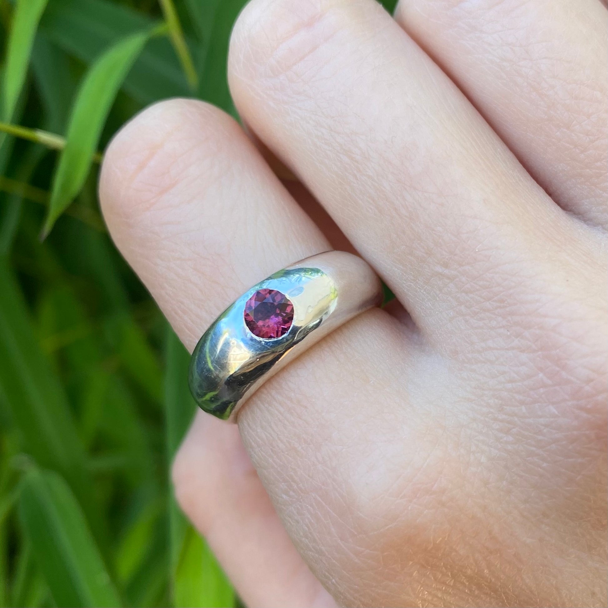 Chunky silver ring set with a pink garnet shown on a hand