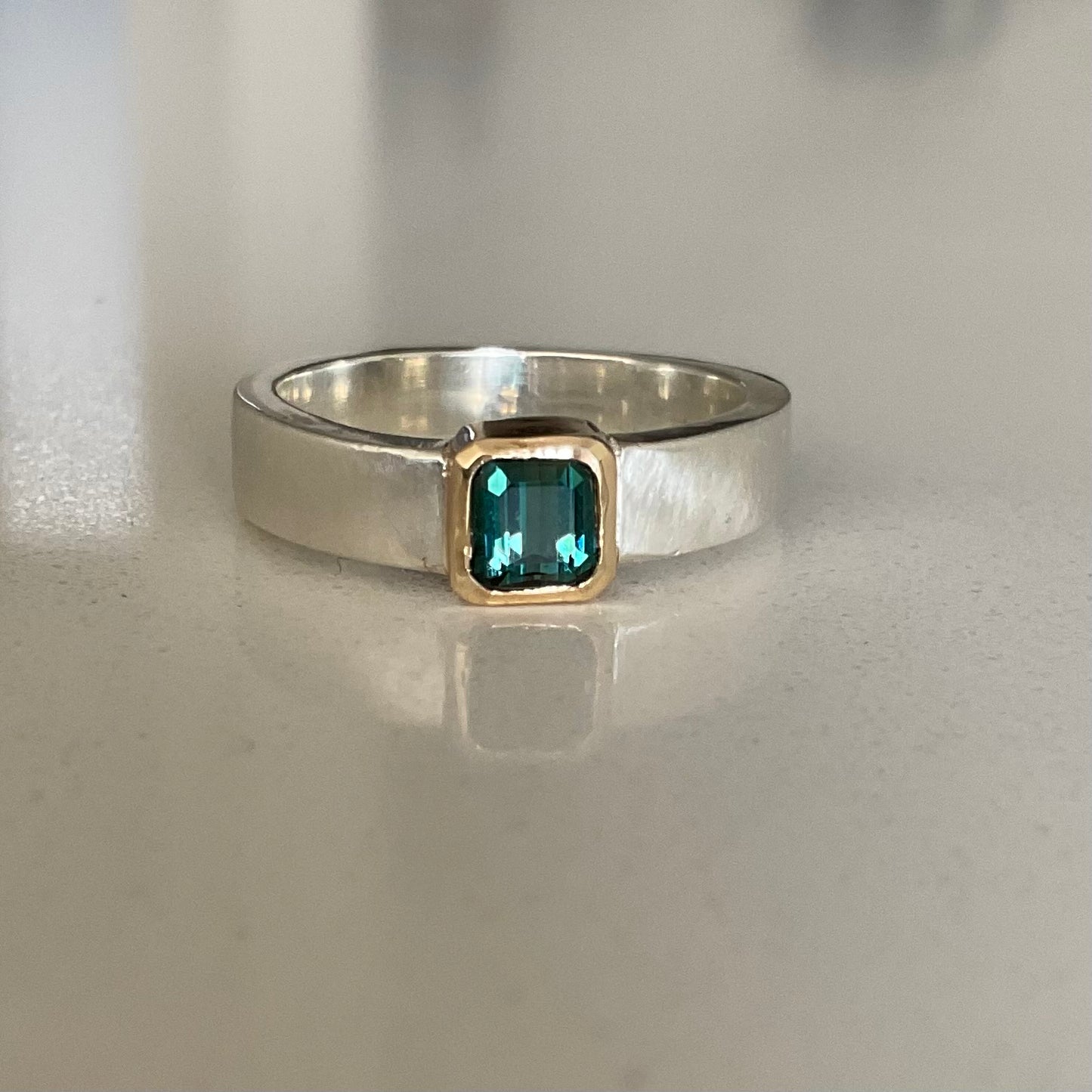 Silver ring with a green gemstone on a reflective surface