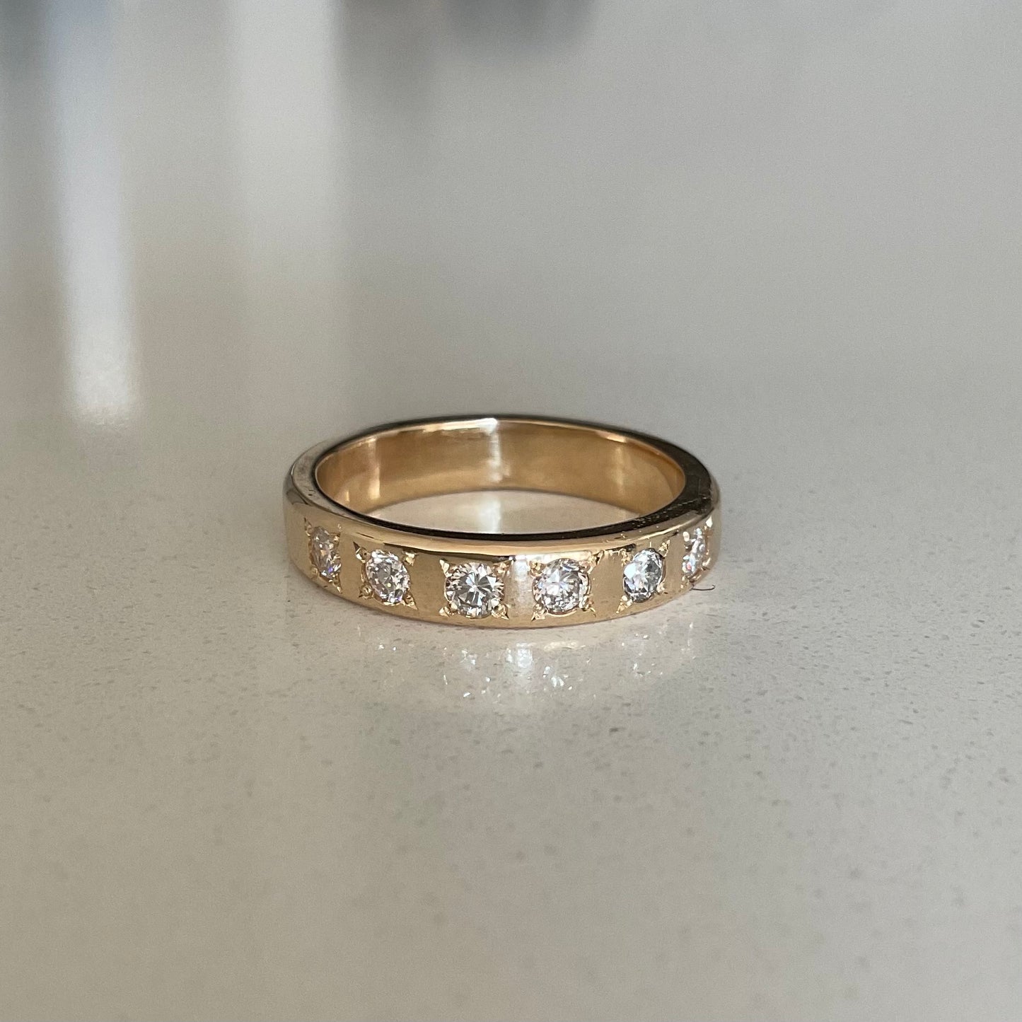 Gold ring with embedded diamonds on a light gray surface