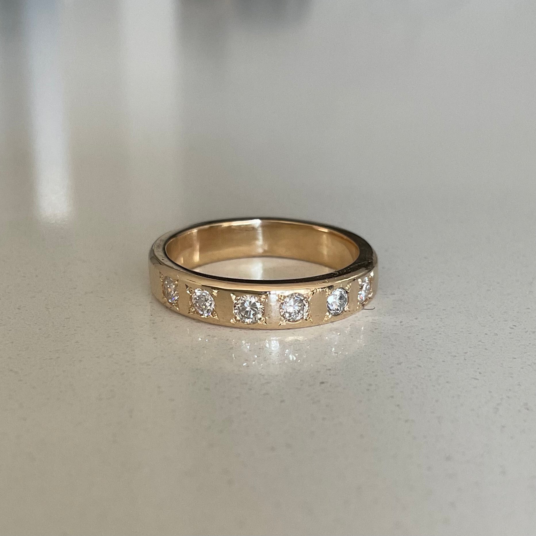 Gold ring with embedded diamonds on a light gray surface