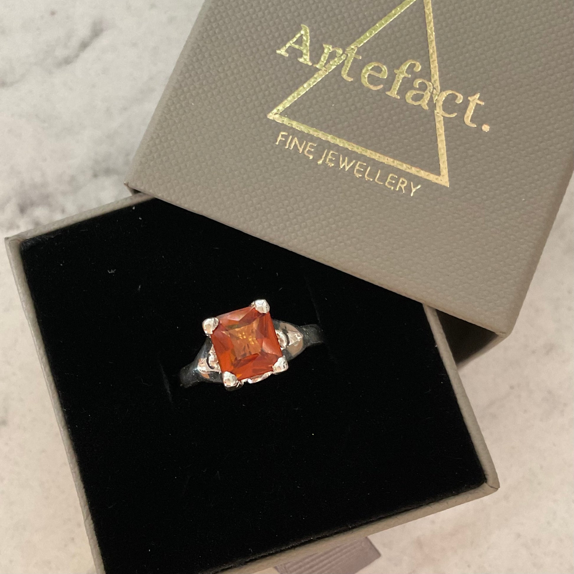Square-cut gemstone ring in a 'Artefact' jewelry box on a marble surface
