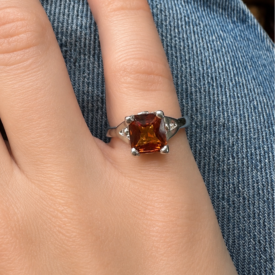 Ring with an orange Fanta garnet gemstone on a person's finger against a denim background